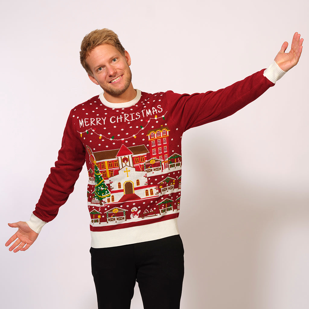 En mand poserer med armene ud til siden i en rød julesweater.